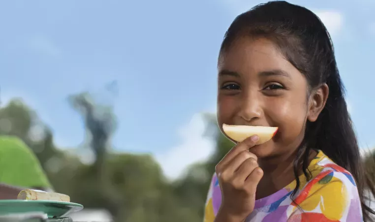 Child using an apple slice to mimic a smile